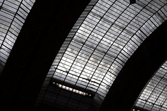 Upward view of a dramatic glass roof with geometric steel framing and massive dark arches in Paris, France.