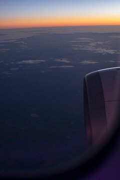 Airplane engine above the clouds at sunset, viewed through a passenger window in flight