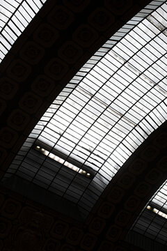 Upward view of a dramatic glass roof with geometric steel framing and massive dark arches in Paris, France.