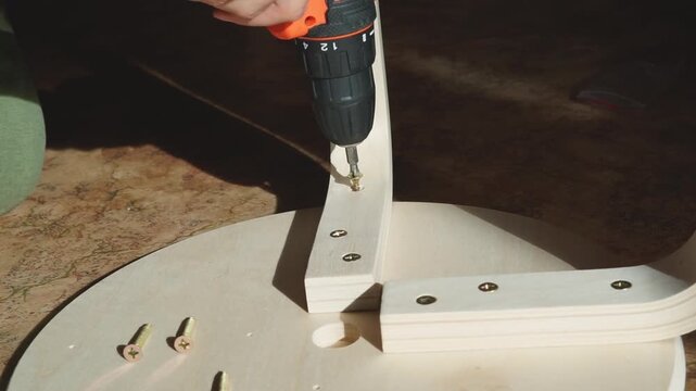 DIY furniture assembly, cordless drill screwing wooden stool leg close up