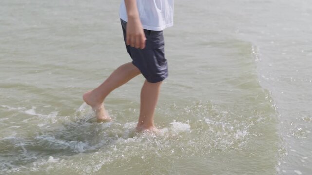 Close-up of a boys legs splashing through shallow sea water an unrecognizable child