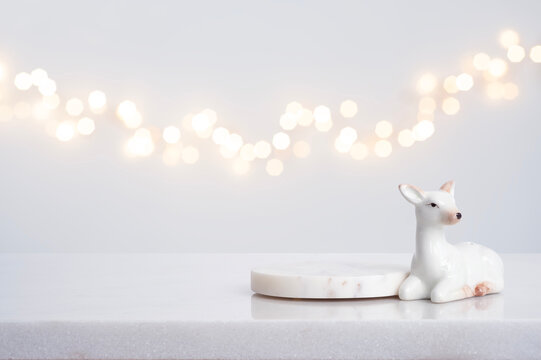 White ceramic deer and marble round coaster for product display against abstract blurred holiday garland lights background