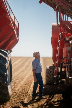 Farmer inspects large harvesting machinery in a cultivated field.