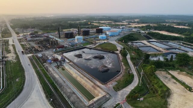 Aerial view of an industrial oil refinery plant with large storage tanks, piping systems, and processing facilities under a glowing sunset sky. Energy, fuel production, and industry concepts.
