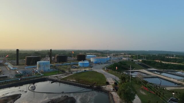 Aerial overview of an energy production site featuring cylindrical storage tanks and waste management ponds under soft daylight. Petroleum industry, fuel distribution, and infrastructure.