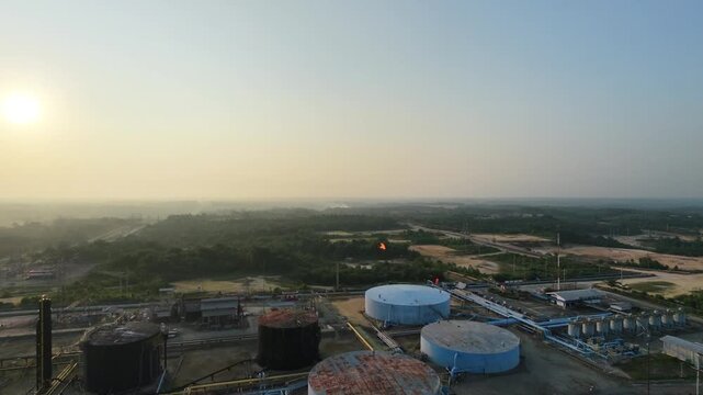 Aerial overview of an energy production site featuring cylindrical storage tanks and waste management ponds under soft daylight. Petroleum industry, fuel distribution, and infrastructure.
