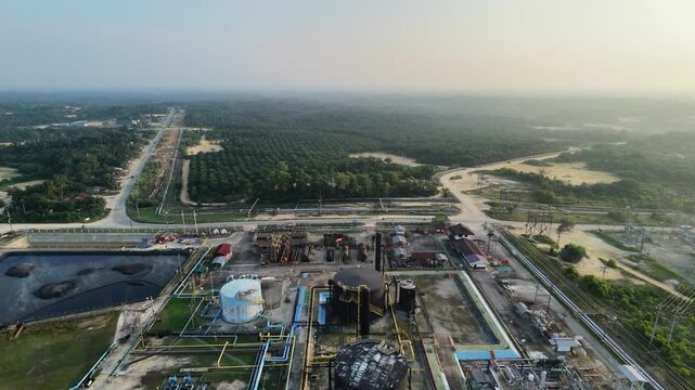 Panoramic aerial view of a sprawling petroleum facility and energy plant during twilight. Includes distinct blue and black storage silos, processing units, and a series of industrial wastewater lagoon