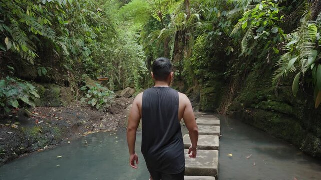 Person Walking Along a Stone Path Across a Natural Pool Surrounded by Lush Tropical Forest at Ulu Petanu Waterfall, Bali, Indonesia