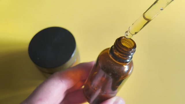 Hand holding an amber dropper bottle with cosmetic serum for topical skincare use.