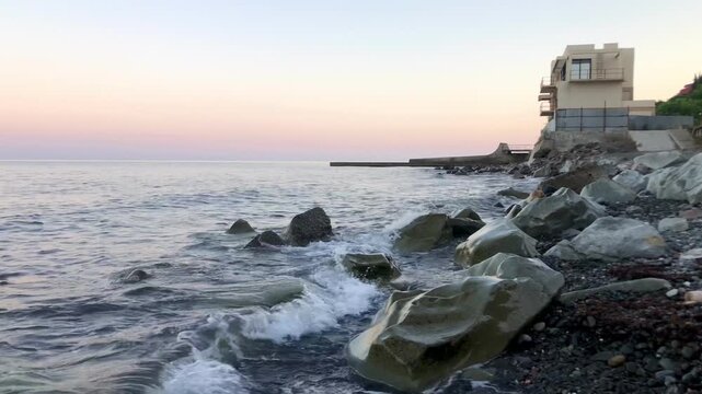 A coastal scene at twilight, likely dawn or dusk, featuring a rocky shoreline.