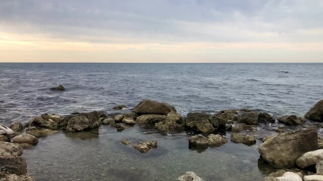 A coastal scene featuring a rocky shoreline that forms a small, natural tidal pool in the foreground. 