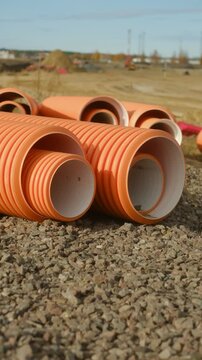 Orange corrugated plastic pipes for plumbing and drainage systems lying on pile of gravel large outdoor construction site, ready for installation underground for new development project. Vertical shot