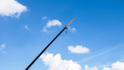 The boom construction crane against bright blue sky with fluffy white clouds. © ALEXEY