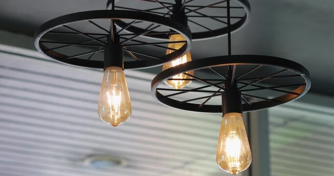 Industrial style ceiling pendant lights with black metal wheel frames and glowing Edison bulbs, creating a warm vintage atmosphere for modern cafe, restaurant and home interiors