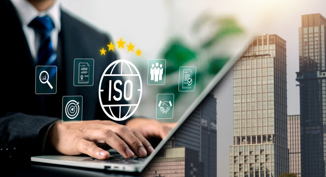 Businessman using a laptop with glowing ISO standard certification icon and quality management symbols over a city background. Concept of business compliance, quality assurance, and standard.