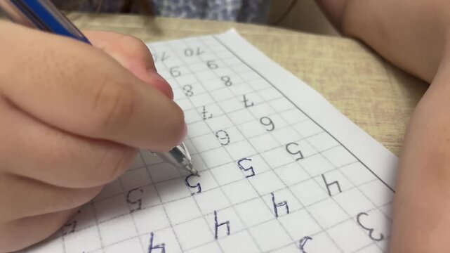 Macro close up of child hand writing numbers in grid notebook with ballpoint pen during elementary math lesson home study stock footage.
