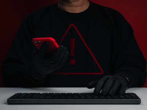 Cybercriminal using smartphone and keyboard with red warning symbol. Mobile account takeover, unauthorized access, compromised credentials, hacking, cyber fraud, and digital security threats concepts.