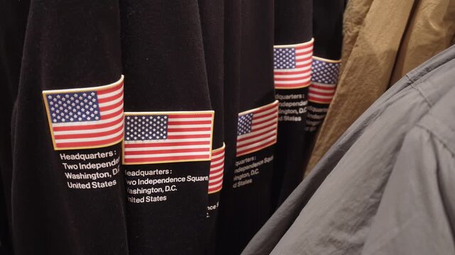 Many hoodies with sewn rubber flags on sleeve of black fleece sweatshirt hang on rack in store. 3D patches decorate branded American national apparel in clothing shop.