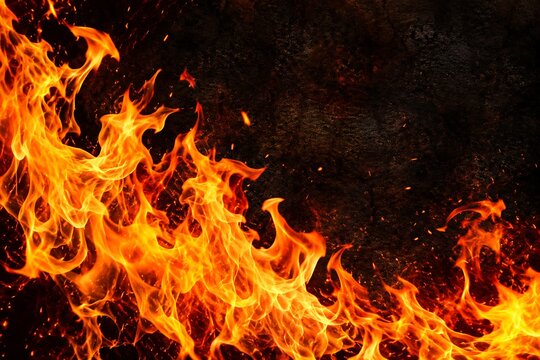 Bright orange and yellow fire flames burning with glowing sparks on a dark black background