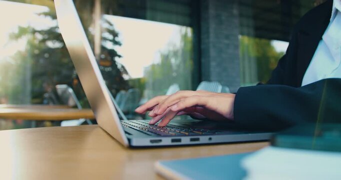 View of woman hands typing on laptop keyboard while sitting on bench on street, focused on business task