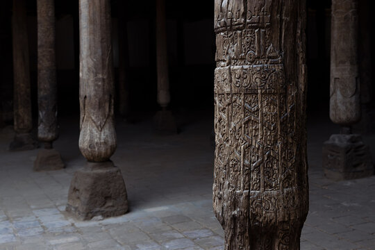 Carved wooden columns inside Juma Mosque in Khiva with intricate geometric and floral patterns on aged wood. Ideal for travel publications, heritage content, and cultural documentation.
