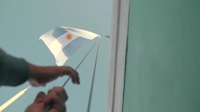 Hand hoisting a small Argentine flag outdoors in Argentina.