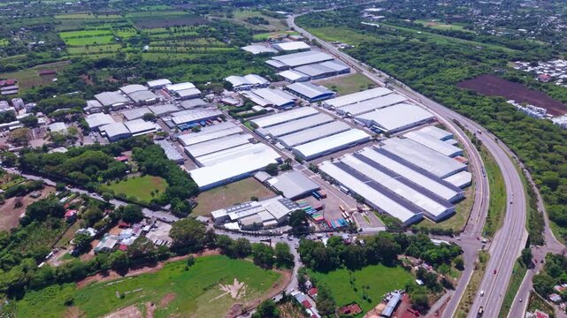 A high-altitude drone tracking shot over the expansive free trade zone industrial park in Tamboril, Santiago, showing warehouses, manufacturing facilities, and adjacent highway