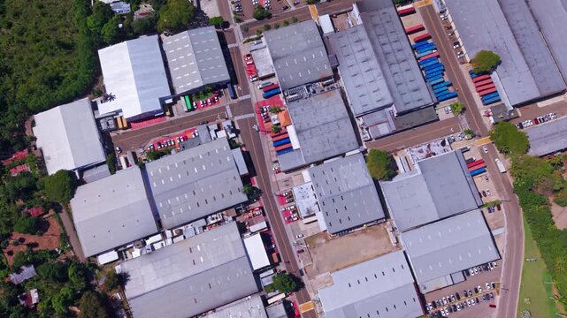 An overhead vertical drone shot tracking across modern manufacturing facilities, large warehouses, and streets in the industrial zone of Tamboril, Santiago