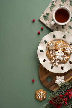 Cozy winter holiday scene with gingerbread cookies, steaming tea, pine branches and festive decorations on vertical green background with copyspace
