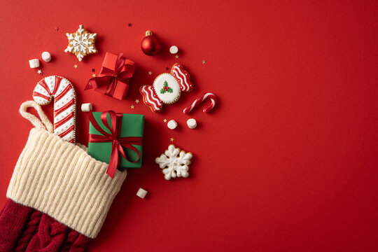 Merry Christmas stocking filled with gifts, cookies, candy and ornaments for Happy New Year celebration on red background with copy space