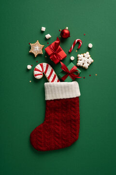 Red Christmas stocking filled with gifts, candy cane, cookies, ornaments and bows for Merry Christmas and Happy New Year on vertical green copyspace