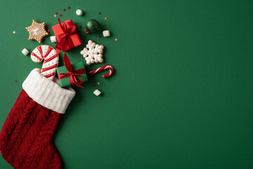 Red knit Christmas stocking filled with gifts and cookies on green background Merry New Year on banner empty space fot greetings © ActionGP
