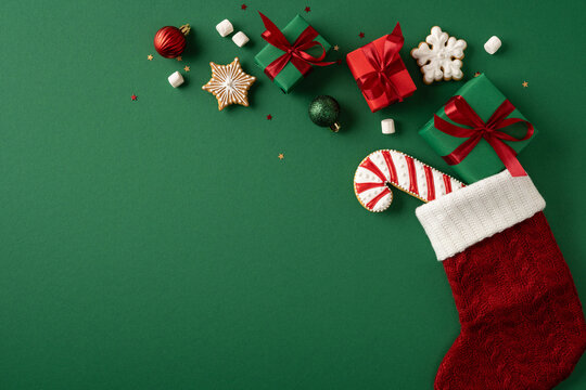 Red Christmas stocking with gifts, candy cane and cookies on poster wide green background celebrating Merry Christmas Happy New Year