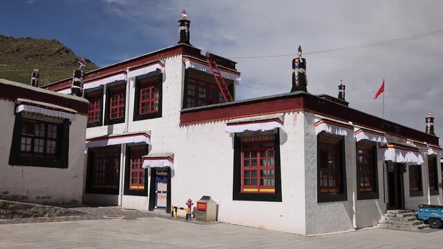 View of the traditional white architecture of Tashilhunpo Monastery with red window frames and prayer flags in the courtyard, Shigatse, Tibet, China.