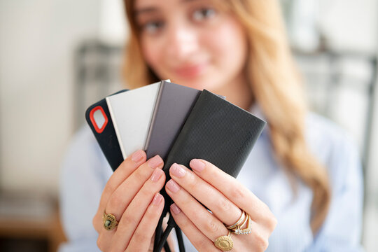 A young woman holds a collection of multiple portable solid-state drives in her hands. She proudly displays the external storage devices toward the camera in an indoor setting.