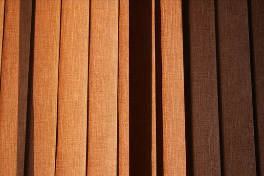 Abstract background of vertical fabric blinds with textured orange and brown stripes in soft indoor lighting