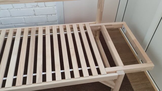 Wooden futon sofa bed frame with slats on a brown rug near white brick wall