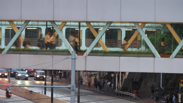 Pedestrians walking through an enclosed glass footbridge with steel truss frames above a busy Hong Kong street, as double-decker buses and cars pass below. Urban commuting and connection.