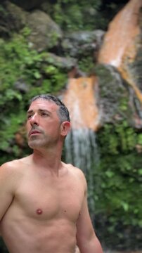 Man relaxing in natural thermal pool waterfall environment