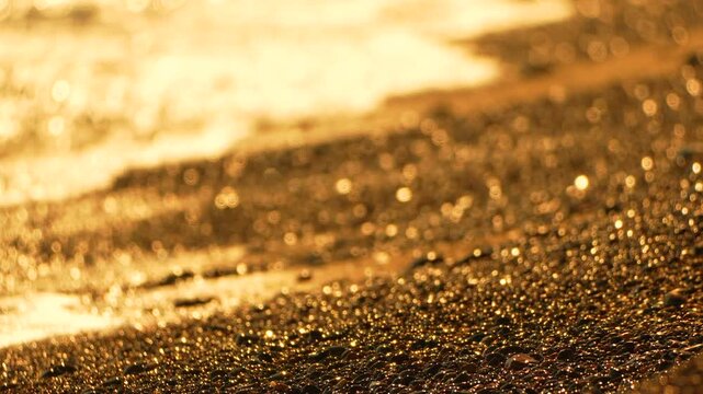 Glistening sea foam rolls over wet dark gravel under the amber glow of sunset. Macro static shot.