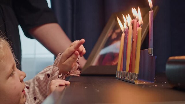 Caucasian child pointing at burning Hanukkah menorah candles during Jewish holiday celebration at home. Footage suitable for holiday advertising, cultural campaigns, or family lifestyle content