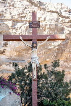 Moqattam neighborhood in Cairo, Egypt. Saint Simon Coptic Monastery. A large crucifix depicting Jesus Christ with a trilingual inscription stands atop the vegetation in front of the rock.