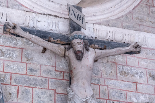 Yonne, Burgundy, France. A polychrome wooden crucifix depicting Christ on the cross with the inscription &ldquo;INRI,&rdquo; mounted on a stone wall at the Saint-Lazare Collegiate Church in Avallon.
