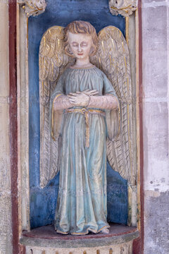 Yonne, Burgundy, France. A polychrome statue of an angel with golden wings and clasped hands in a blue niche at the Church of Saint John the Baptist in Joigny.