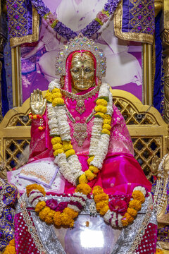 A gilded statue of Mata Lal Devi adorned with flower garlands and jewelry, inside the temple in Amritsar, India.