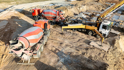 A concrete pump and mixer trucks pour concrete into a foundation at a construction site during the day © Anoo