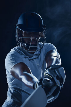 Concentrated helmeted cricketer extending bat forward in dark blue studio closeup. Batting technique, competitive focus concept.