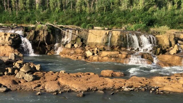 The image shows a wide, cascading waterfall over flat, stepped rocky ledges with a very distinctive, blocky appearance.