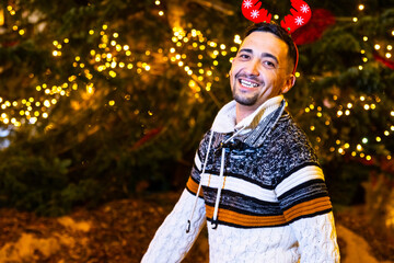Man with reindeer antlers smiling against blurred christmas tree lights, celebrating holidays © Ivi - Powerlightss