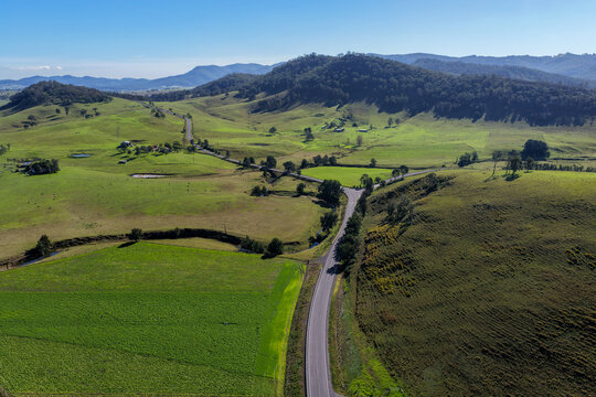 Aerial view of a winding rural road crossing green farmland below wooded hills in Lambs Valley, Hunter Valley, New South Wales, Australia.